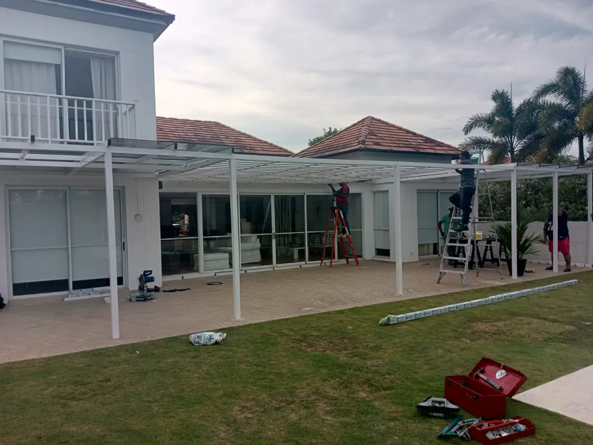 Instalación de una pérgola blanca con techo de vidrio en una casa